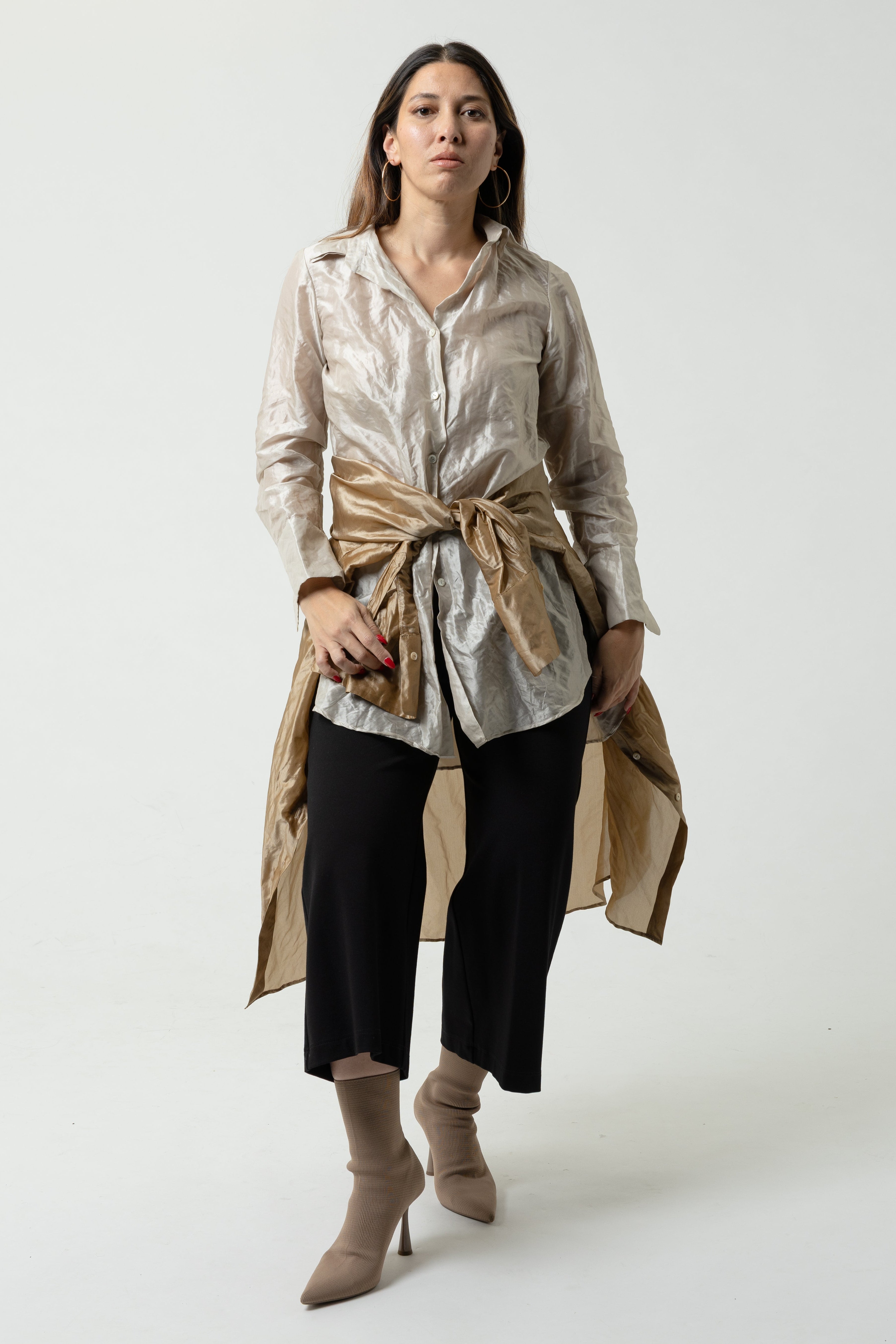 Woman wearing a beige trench coat over a white shirt with black pants on a white background