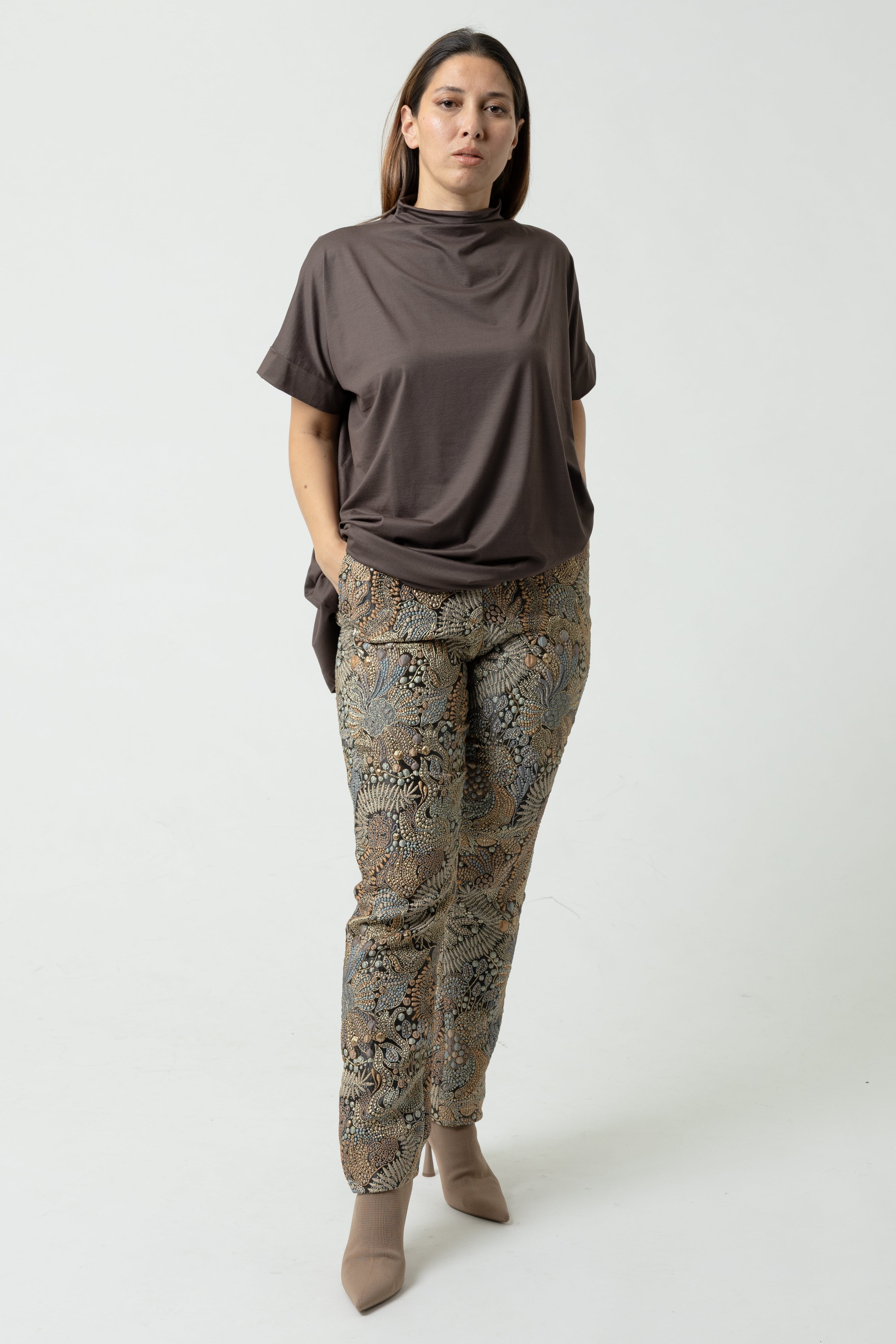 Woman wearing a brown top and patterned pants on a white background