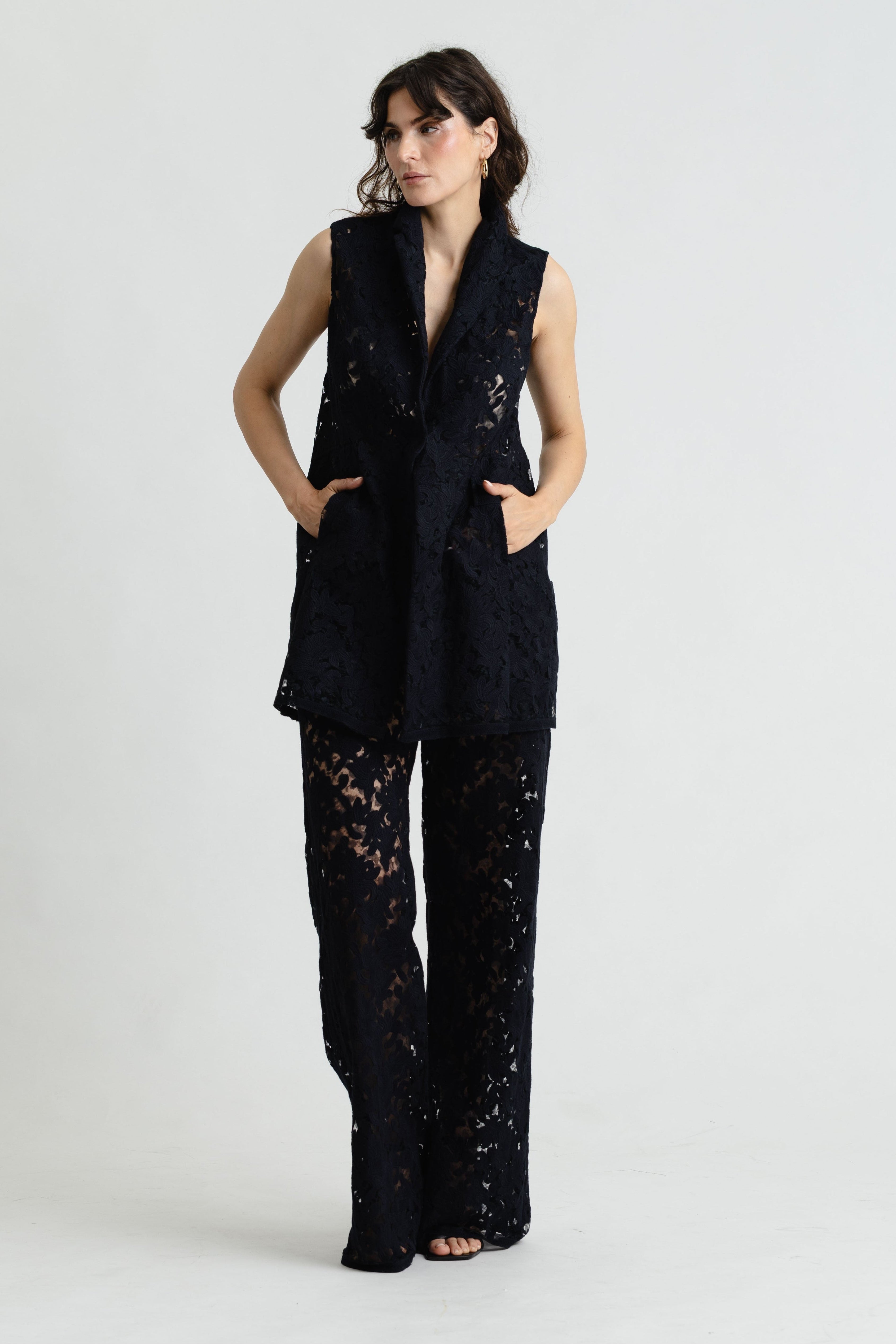 Woman wearing a black sleeveless top and lace pants on a white background