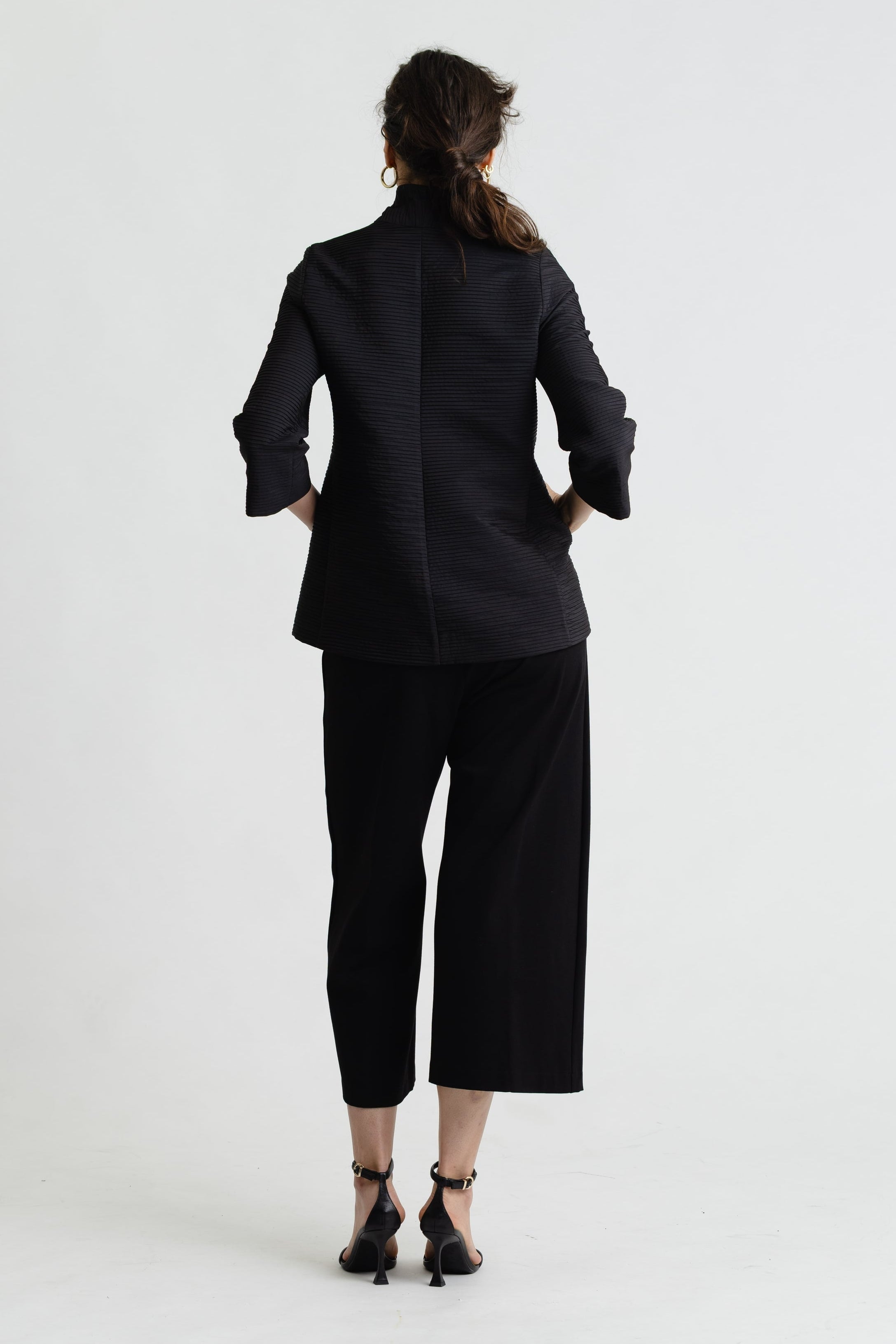 Person wearing a black suit standing against a white background