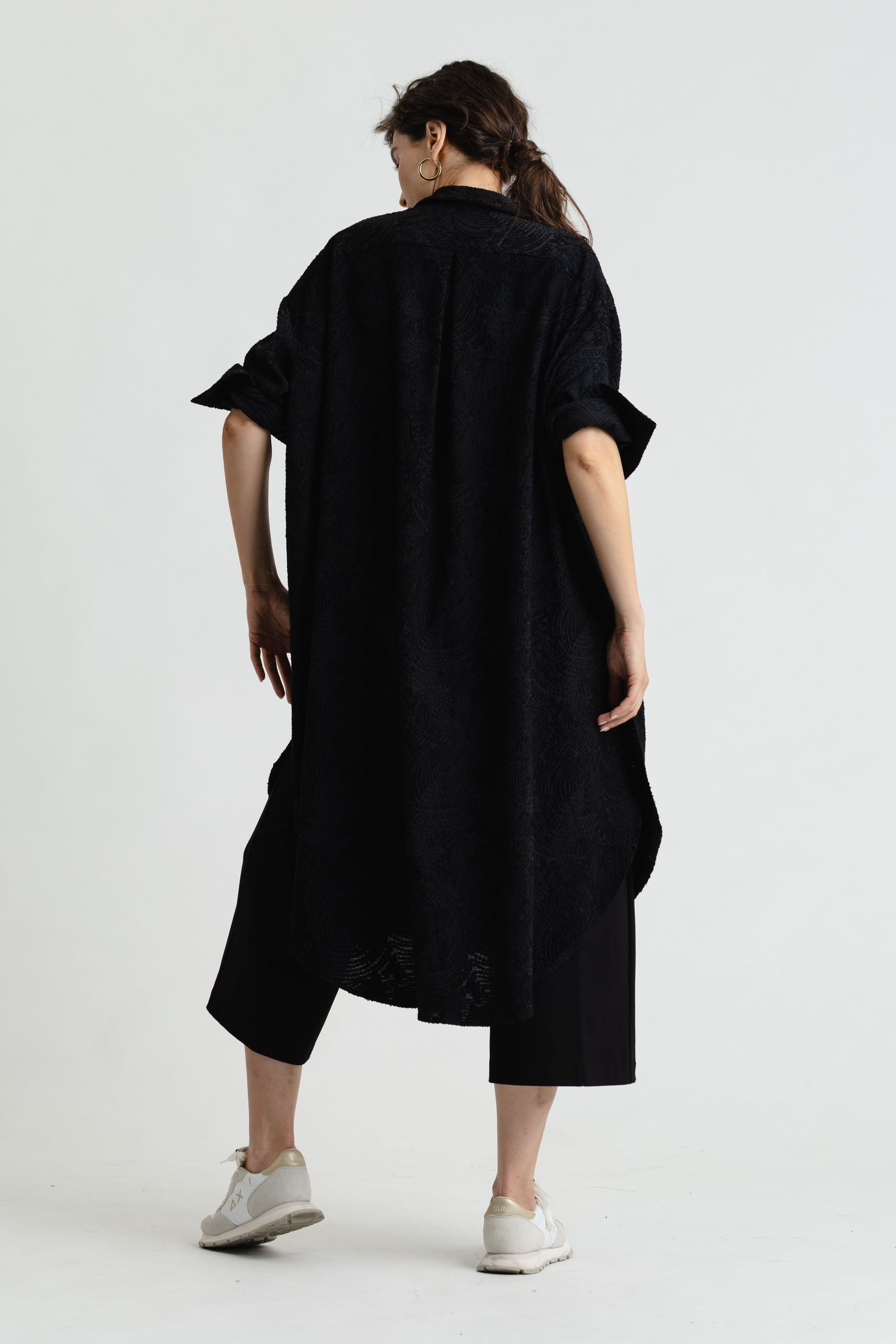 Person wearing a black dress with rolled-up sleeves on a white background