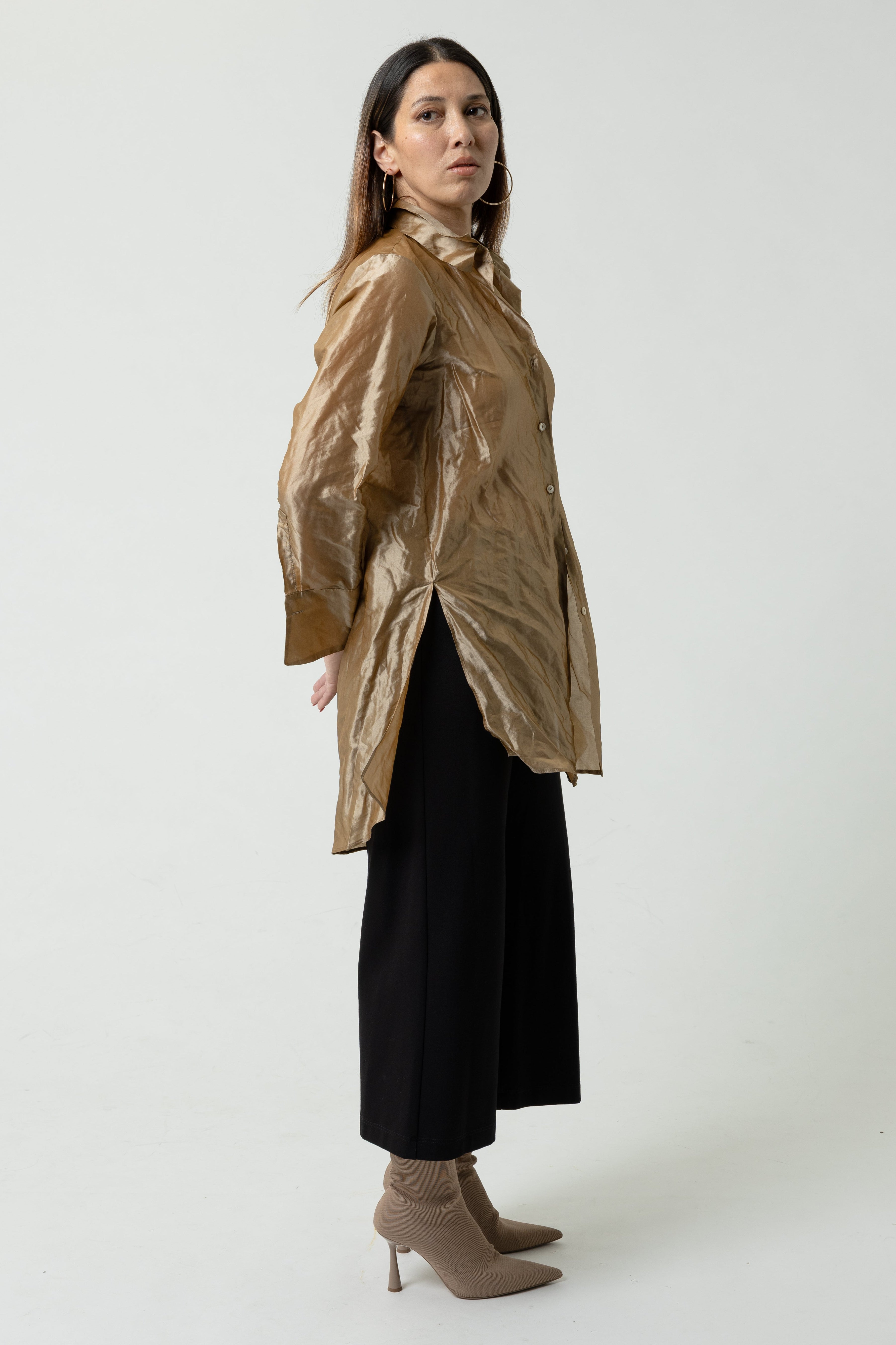 Woman wearing a gold jacket and black pants on a white background