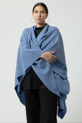 Woman wearing a blue shawl over a black outfit on a white background
