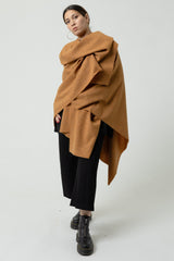 Person wearing a brown poncho over a black outfit on a white background