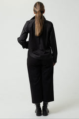 Person wearing a black outfit standing against a white background