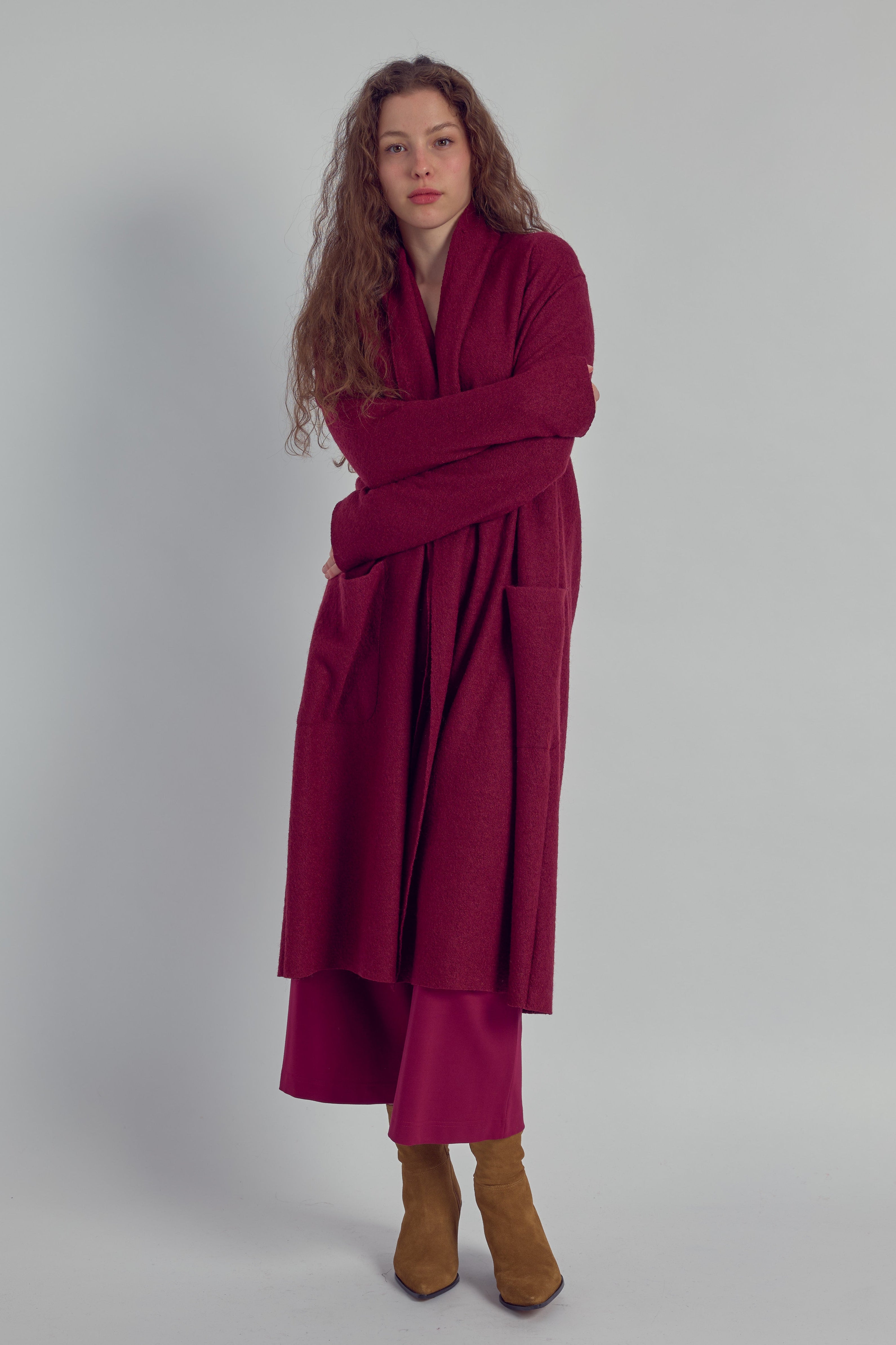 Woman wearing a long burgundy cardigan, with a matching trousers on a plain background