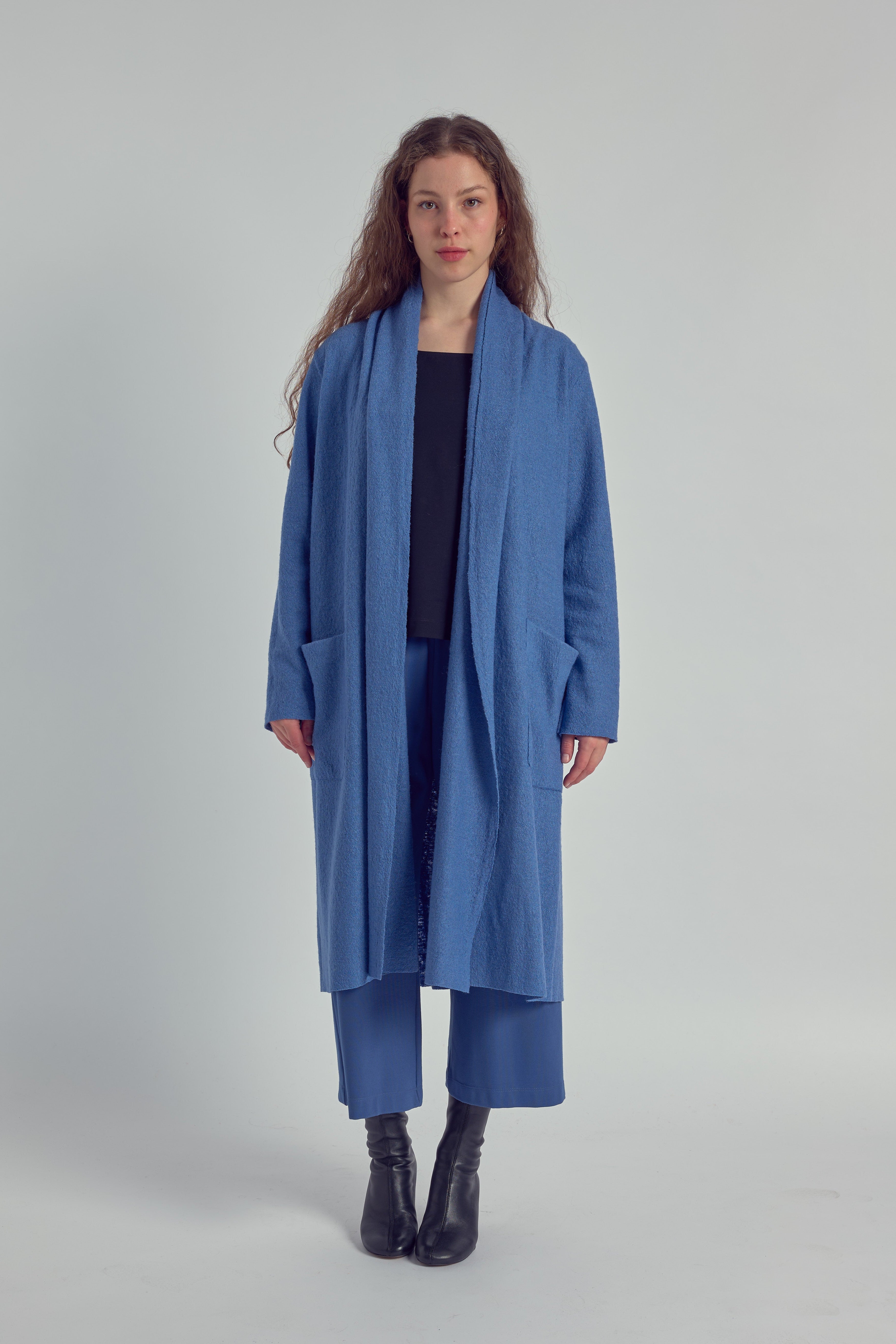 A woman is wearing a long sky blue cardigan, with a matching trousers, and a navy blue shirt, on a plain white background.