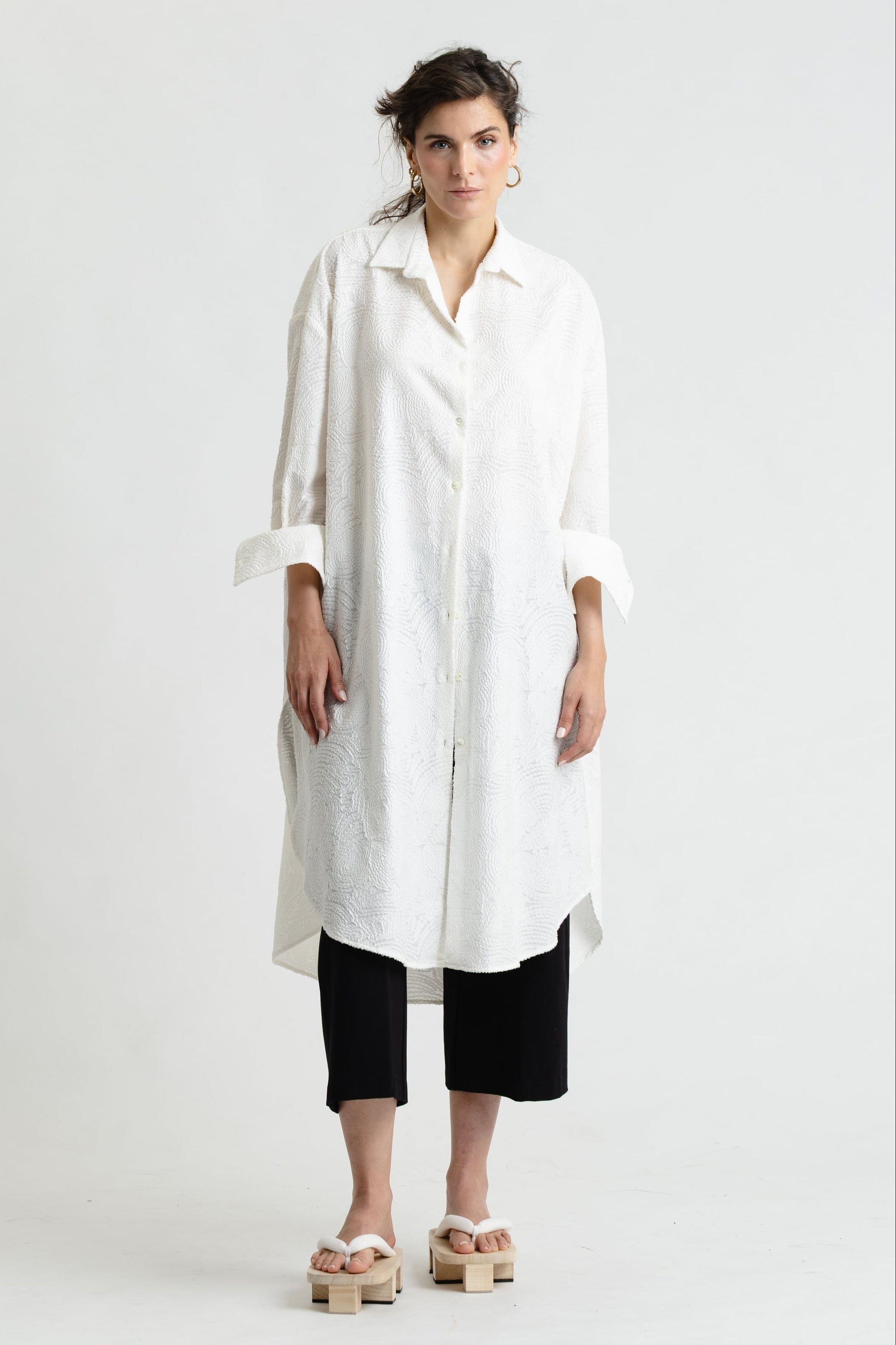 Person wearing a long white shirt and black pants on a white background