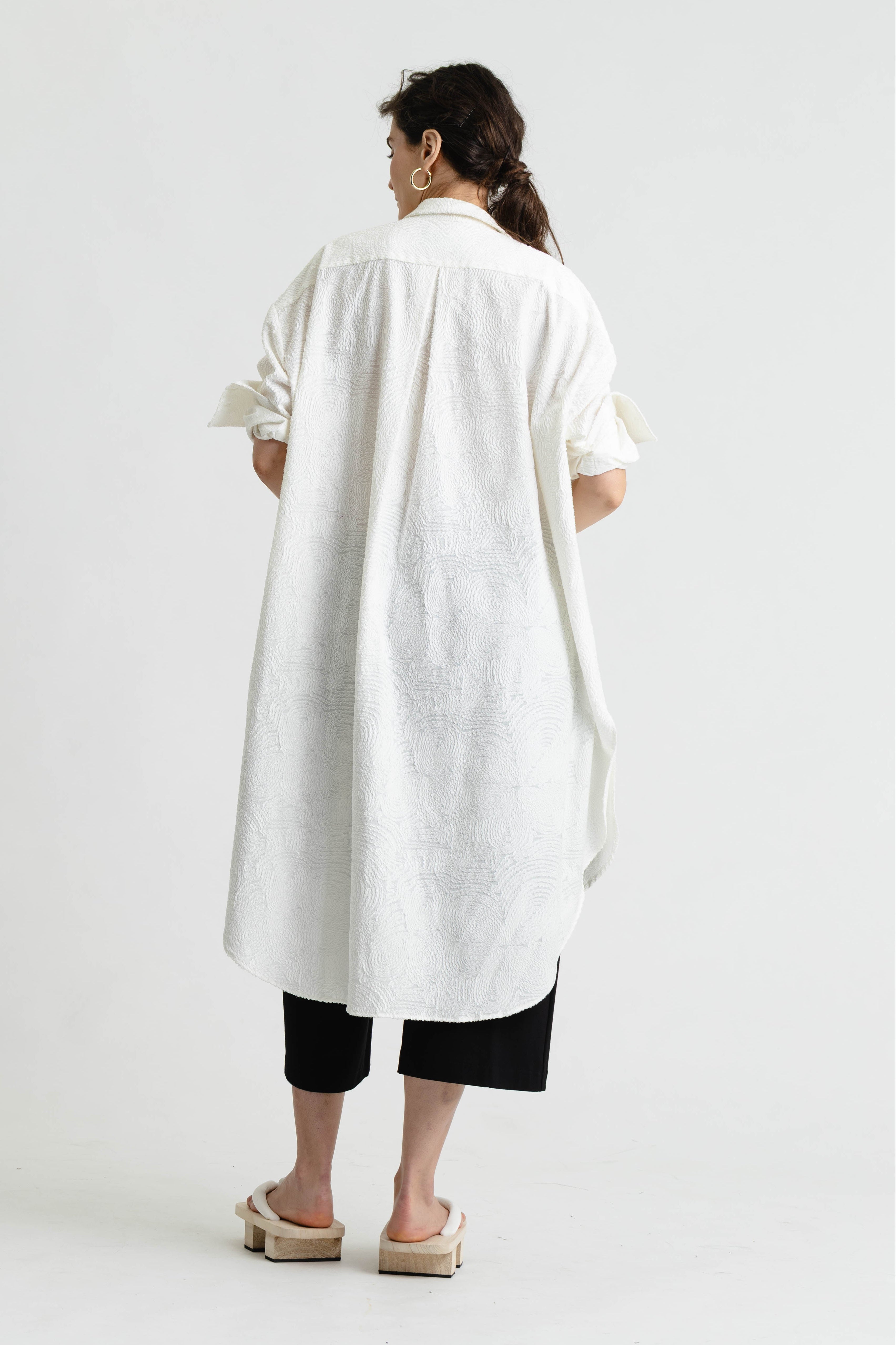 Person wearing a long white shirt and black pants on a white background