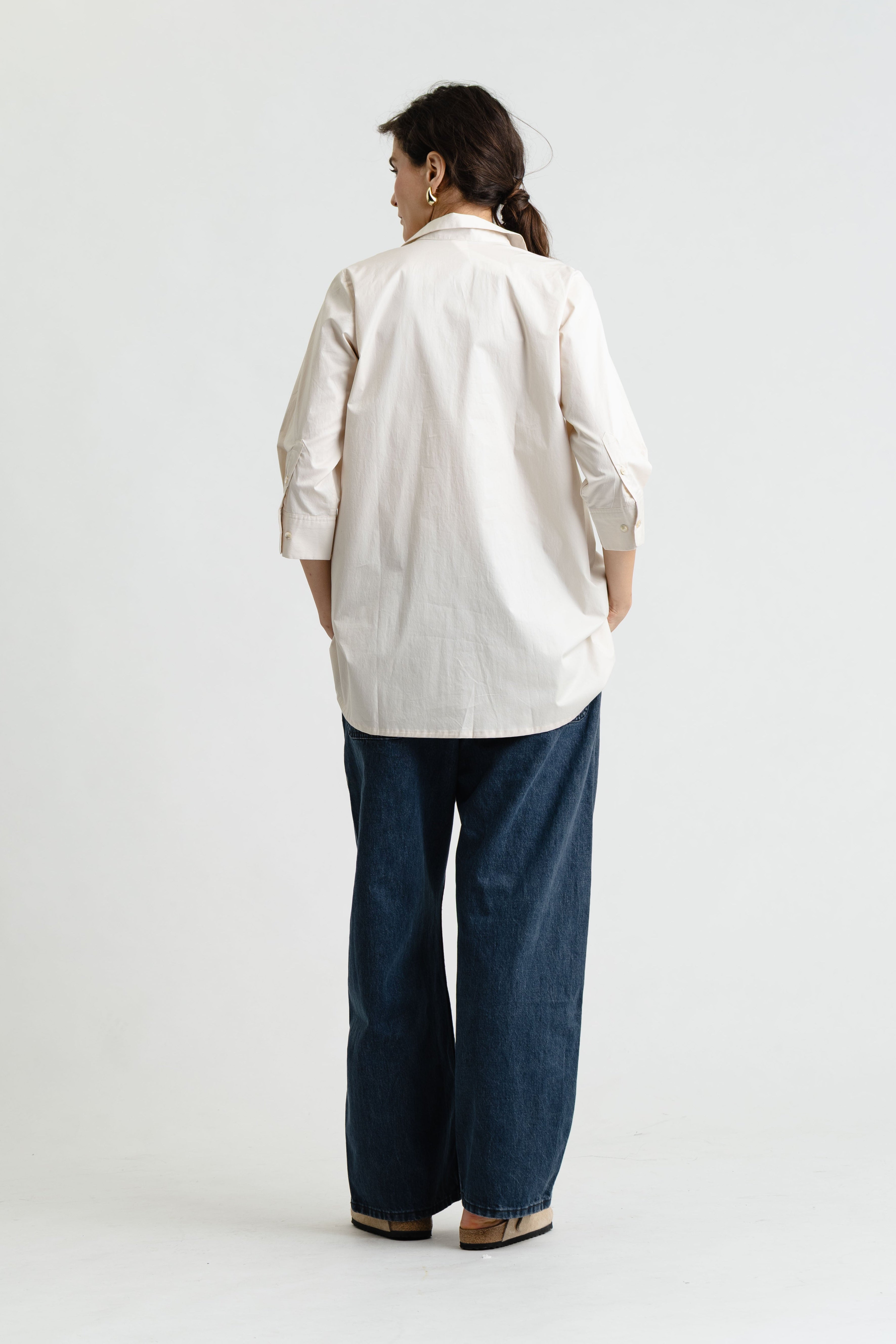 Person wearing a beige shirt and blue pants on a white background