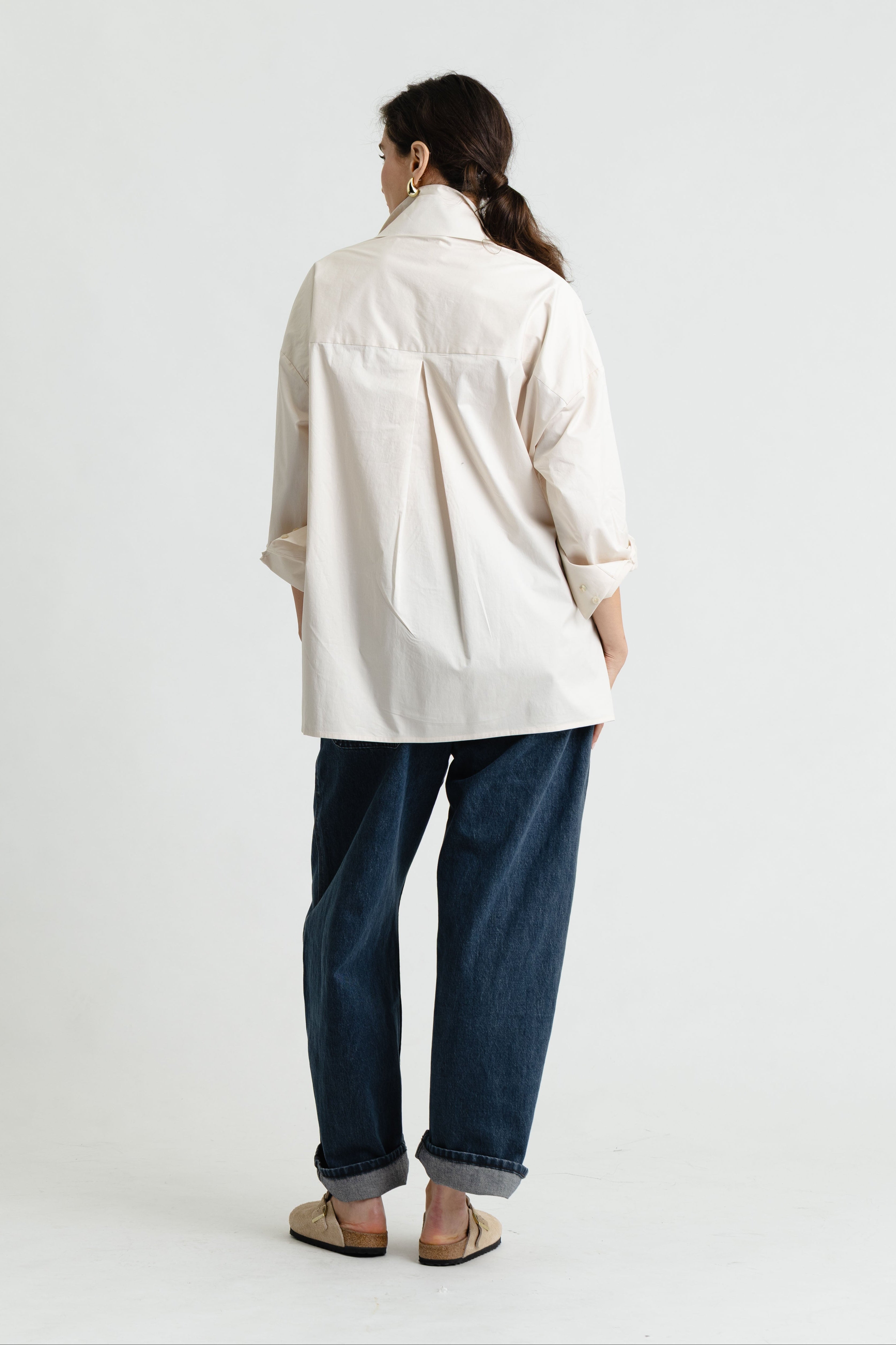 Person wearing a light-colored coat and dark jeans on a white background