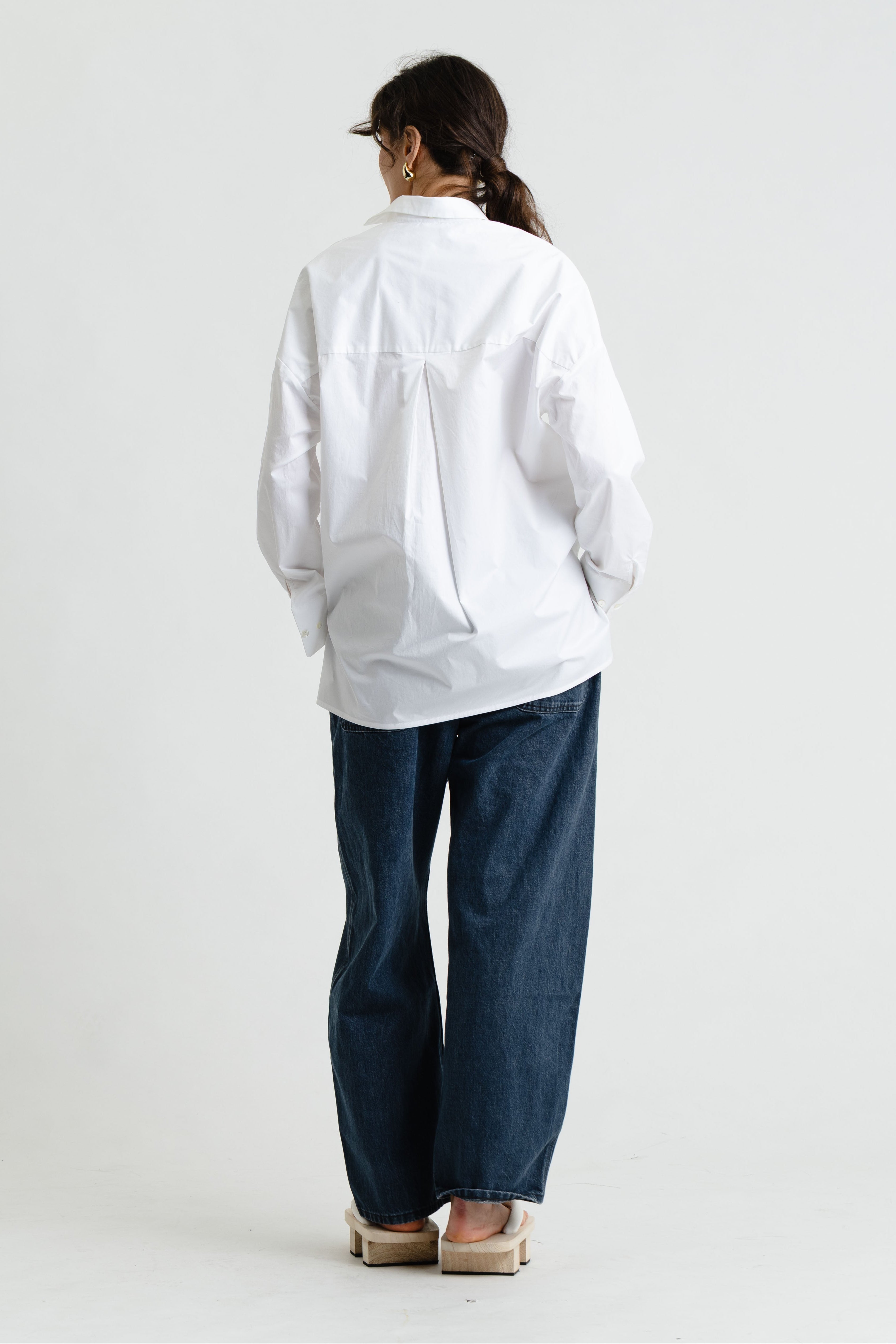 Person wearing a white shirt and blue pants on a plain background
